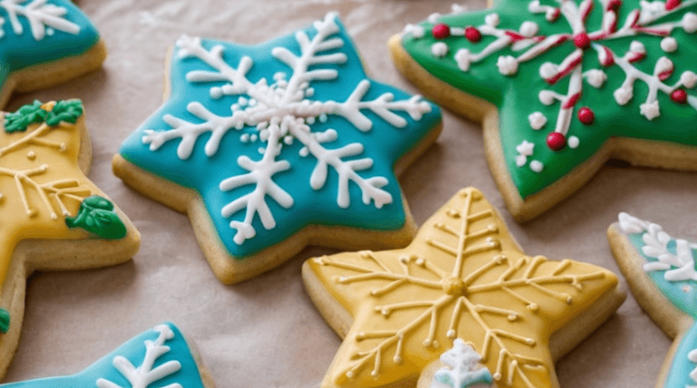 A festive scene of freshly baked Christmas sugar cookies on a decorative plate, decorated with colorful icing, sprinkles, and edible glitter. The background includes Christmas decorations like a tree and lights, creating a warm, cozy holiday atmosphere.